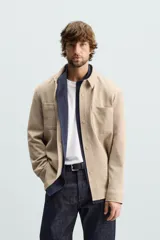 Sobrecamisa negra de tejido con elasticidad, cuello solapa, manga larga con puño abotonado, bolsillos de plastrón en el pecho y cierre frontal con botones a presión.