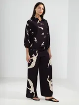 Camisa de manga 3/4 con puños elastizados, cuello camisero y estampado de figuras humanas y peces en color crema sobre fondo negro.