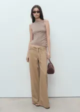 Pantalón de tiro medio, corte wideleg y largo, color beige. Confeccionado en mezcla de algodón y lino, presenta cinco bolsillos, trabillas, cinturón ajustable y cierre de gancho y cremallera.