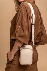 Bandolera pequeña tipo 'phone bag' de símil cuero color rosado pálido, con cierre de cremallera y correa ancha de tela con diseño de chevron en tonos claros.