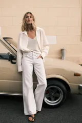 Camisa blanca de algodón con cuello solapa, manga larga con puños abotonados, bolsillo de parche en el pecho, bajo redondeado y cierre frontal con botones.