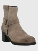 Bota corta de cuero color taupe, con caña de 14 cm, taco cuadrado de 6 cm y punta cuadrada. Presenta una correa con hebilla metálica alrededor del tobillo y cierre lateral.