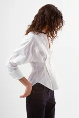 Camisa de manga larga color azul con finas rayas verticales blancas. Presenta cuello mao, botones frontales y dos bolsillos de parche con tapa en el pecho. La prenda tiene un diseño ajustado en la cintura con pinzas y un volumen holgado en las mangas.