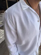 Camisa blanca de fibrana con cuello clásico, manga larga con puños arremangados y cierre frontal con botones de madera.