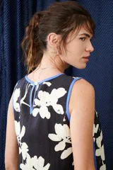 Top sin mangas de color blanco con escote en V y diseño holgado. Presenta un estampado artístico frontal en tonos azul y rojo, con terminaciones de vivo a contratono en color marrón.