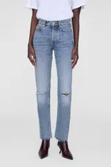 Jean celeste de tiro alto, corte recto y ajustado al tobillo, con roturas en las rodillas y terminación desflecada.