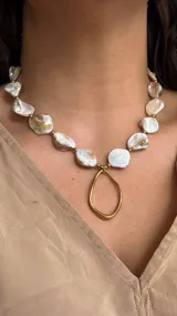 Collar corto con perlas de nácar irregulares y detalles de cuentas doradas. Presenta un dije colgante con forma de aro irregular dorado.