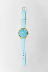 Reloj de pulsera con caja dorada, esfera celeste con indicadores de hora en forma de puntos y agujas doradas. La correa es de cuero celeste.