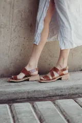 Sandalias de cuero color marrón con tiras cruzadas, taco de 4cm y cierre con hebilla metálica ajustable en el tobillo.