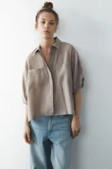 Camisa azul de cuello solapa y manga corta con dobladillo. Tiene dos bolsillos de parche en el pecho, bajo asimétrico con aberturas laterales y cierre frontal con botones ocultos.