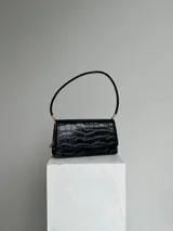 Cartera negra de hombro con textura tipo cocodrilo, doble compartimento interno, dije metálico con la letra B y cierre con broche imán.