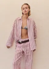 Camisa oversize de manga larga, cuello camisero y cierre frontal con botones. Presenta un estampado de rayas verticales finas en tonos rosa pálido y negro/gris oscuro.