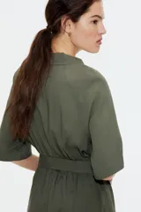 Vestido midi color verde oliva con cuello camisero, botonadura frontal y mangas raglán cortas. Tiene elástico fino en la parte posterior de la cintura, frunces adelante y atrás, y cinturón extraíble para atar.