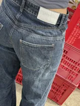 Pantalón jean azul oscuro, de corte wide leg y tiro medio. Presenta detalles de costuras diagonales en la parte superior.