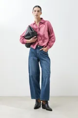 Camisa fucsia de manga larga con cuello camisero y cierre frontal con botones. Presenta apliques de estrellas bordadas en el frente y en el cuello.