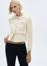 Chaqueta corta color crema de tweed con cuello redondo, cierre frontal con botones metálicos, cuatro bolsillos de parche delanteros, terminaciones deshilachadas y forro interior.