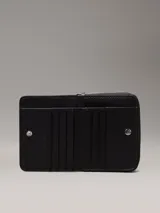 Billetera mediana negra con cierre perimetral y textura de monograma en relieve. Presenta el logo metálico de Calvin Klein en el frente y herrajes plateados.