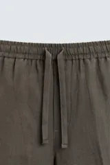 Pantalón de lino color marrón oscuro, de corte recto y relaxed fit. Tiene cintura elástica ajustable con cordón, bolsillos frontales y traseros de parche.