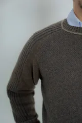 Sweater marrón de lana lambswool con cuello redondo y mangas largas. Presenta un diseño de punto texturizado en el cuerpo y mangas con detalle de punto acanalado en hombros y puños.