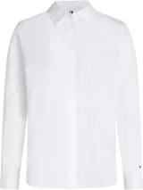 Camisa blanca de corte regular, confeccionada en popelín de algodón orgánico, con cuello inglés, puños con botón, bajo redondeado y logo de Tommy Hilfiger bordado en el pecho.