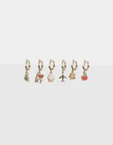 Set de seis aros dorados con argolla y dijes esmaltados: oso de peluche, corazón con texto "I Love NY", cupcake, avión, corona y manzana.