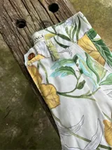 Pantalón corto de vestir color crudo con estampado de hojas verdes y amarillas.