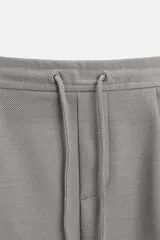 Bermuda color beige de corte recto, con cintura elástica ajustable con cordón, detalle de pliegues frontales, bolsillos laterales y bolsillos de vivo en la espalda.