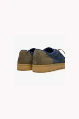 Zapatillas urbanas Satorisan modelo Heisei Suede 1.0, color azul marino, con capellada de gamuza. Presentan suela de goma color caramelo y detalles en verde lima en los cordones. El talón tiene un parche de refuerzo en color verde oliva.