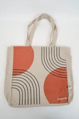 Bolso tote de tela con estampado de rayas verticales rosadas y blancas, laterales y asas en color beige. Presenta la palabra "BONJOUR" en verde en el centro y "INDIAN" en la parte inferior.
