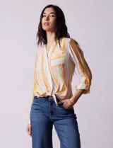 Blusa de gasa estampada a rayas verticales en tonos celeste, lila, naranja y marrón. Tiene cuello a la base con escote en V y botones. Delantera con bolsillo aplicado. Largo de manga regulable con presilla y botón. Terminación anudada opcional.