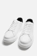 Zapatillas urbanas de cuero sintético negro con cordones y suela blanca de goma con volumen.