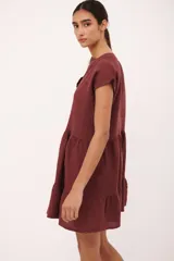 Vestido corto de lino color vino tinto, con escote en V y mangas cortas tipo musculosa. Presenta un corte holgado con volados en el ruedo.