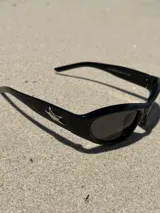 Gafas de sol negras con montura rectangular, lentes oscuras y detalle de estrella plateada en el lateral.