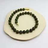 Collar de cuentas esféricas de jade verde, con separadores de hilo lila y cierre de mosquetón dorado.