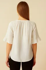 Blusa color blanco de lino y viscosa, con cuello a la base, mangas cortas con volados y cierre frontal con botones.