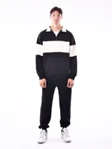 Buzo negro con cuello polo y cierre de cremallera parcial. Presenta una franja horizontal blanca en el pecho y mangas largas.