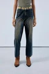 Jean straight de denim azul con recortes en el frente y piedras decorativas, con detalles de desgaste.