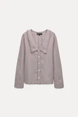 Camisa de manga larga con puños, con cuello bobo con volados y escote en pico. Cierre frontal con botones y estampado de cuadros vichy en blanco y negro.