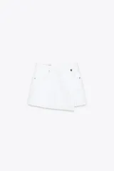 Falda pantalón corta de tiro alto color blanco, con bolsillos delanteros y traseros. Cierre frontal cruzado con cremallera oculta y botón metálico.