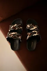 Sandalias bajas sin talón, confeccionadas en cuero negro con apliques de tachas y cuero con estampado animal print.