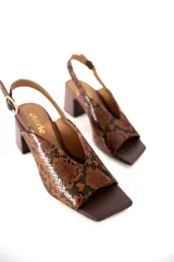 Sandalias Cherie con estampado de piel de serpiente en tonos marrones y negros. Tienen una tira delgada en la parte delantera, una tira ajustable en el tobillo y un tacón cuadrado.