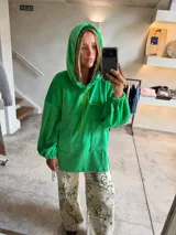 Buzo tipo canguro oversize de tela plush, color azul claro. Presenta capucha, cierre frontal parcial con cordón turquesa y bolsillos canguro frontales. Las mangas son largas y abullonadas con puños ajustados.