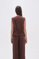 Chaleco negro con finas rayas verticales blancas (pinstripe), escote en V y cierre frontal de botones. Presenta bolsillos ribeteados en la parte inferior delantera.