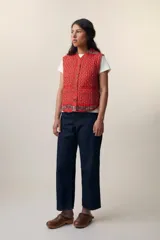 Chaleco sin mangas de algodón acolchado con estampado floral en tonos rojos y marrones. Tiene cuello camisero, cierre frontal con botones de madera y bolsillos de parche. El modelo Patchwork Tomette está tejido a mano.