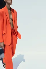Pantalón de vestir color naranja, de tiro alto y pernera ancha. Presenta doble pliegue frontal, trabillas en la cintura, bolsillos laterales y falsos bolsillos de vivo en la espalda.