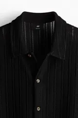 Camisa negra de manga corta con tejido calado tipo crochet, cuello inglés, botones frontales y corte recto.