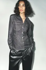 Camisa de denim color gris oscuro, de corte entallado, con cuello solapa, manga larga, dos bolsillos frontales y cierre frontal con botones.