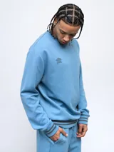 Buzo celeste de corte clásico con logo Umbro bordado en el pecho. Presenta cortes y cambio de color en las mangas, y ribete con rayas grises en cuello, puños y cintura.