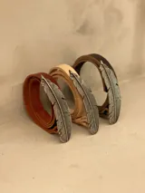 Cinturón de cuero color marrón con hebilla metálica en forma de pluma.