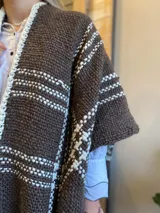 Ruana tejida a mano en tonos marrón y blanco, con flecos en el borde inferior.